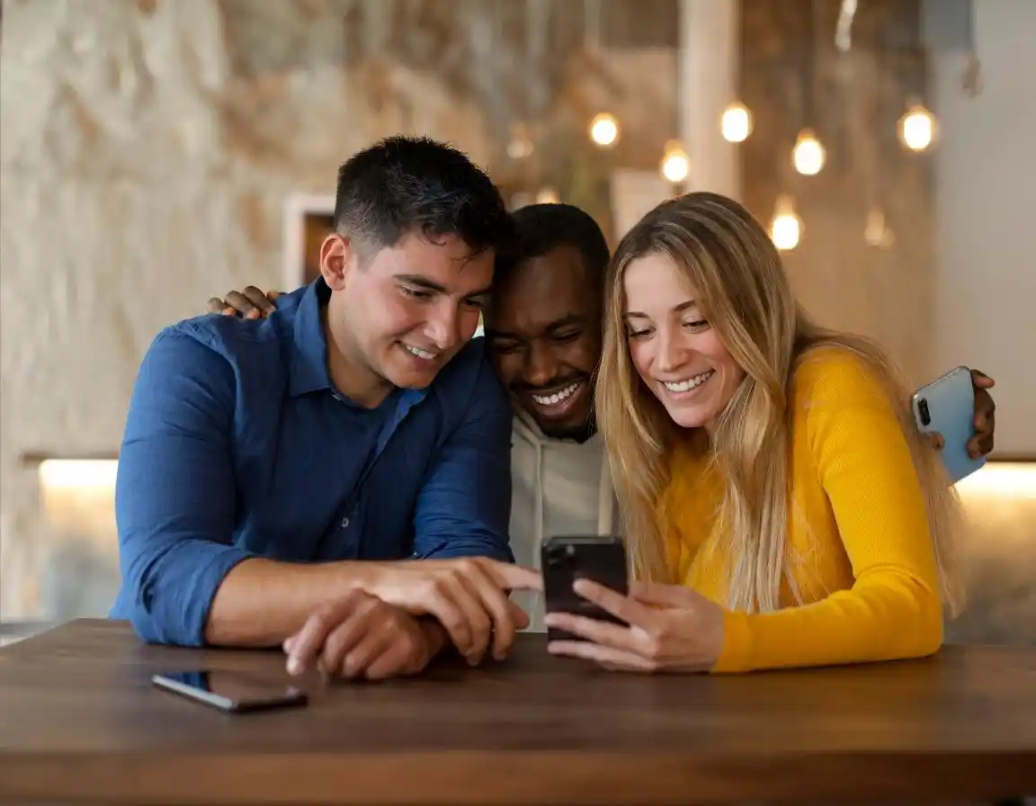 3 friends gathered together at a table using an iphone together
